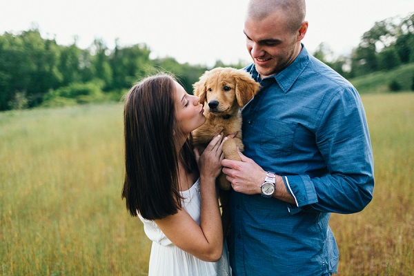 woman in white dress kissing Golden Retriever Puppy that man is holding, on location engagement photos