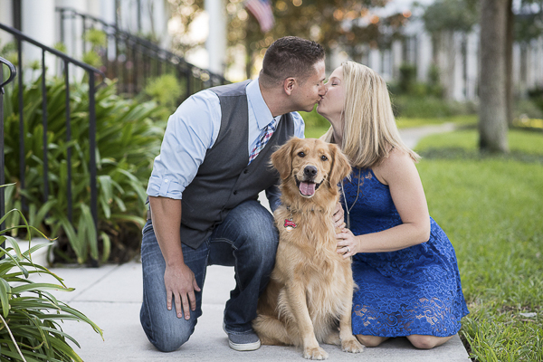 couple kneeling next to dog and kissing