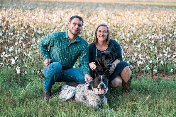 family photo with dogs, black lab mix, Husky/Aussie mix and humans in front of cotton field