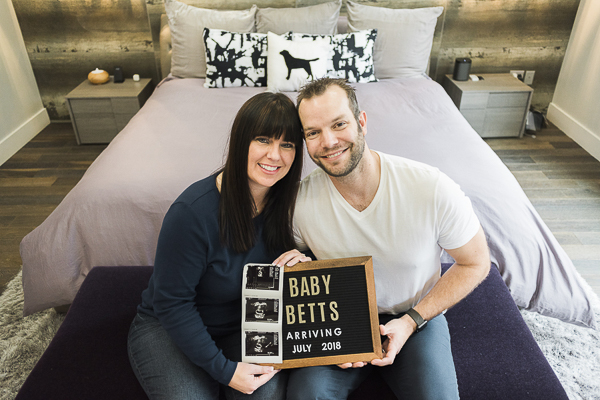couple holding pregnancy announcement sign, sonogram photos, lab pillow in background, dog lovers baby announcement