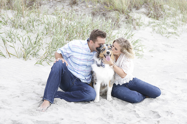 engagement photos with dog, couple kissing their Aussie on the beach