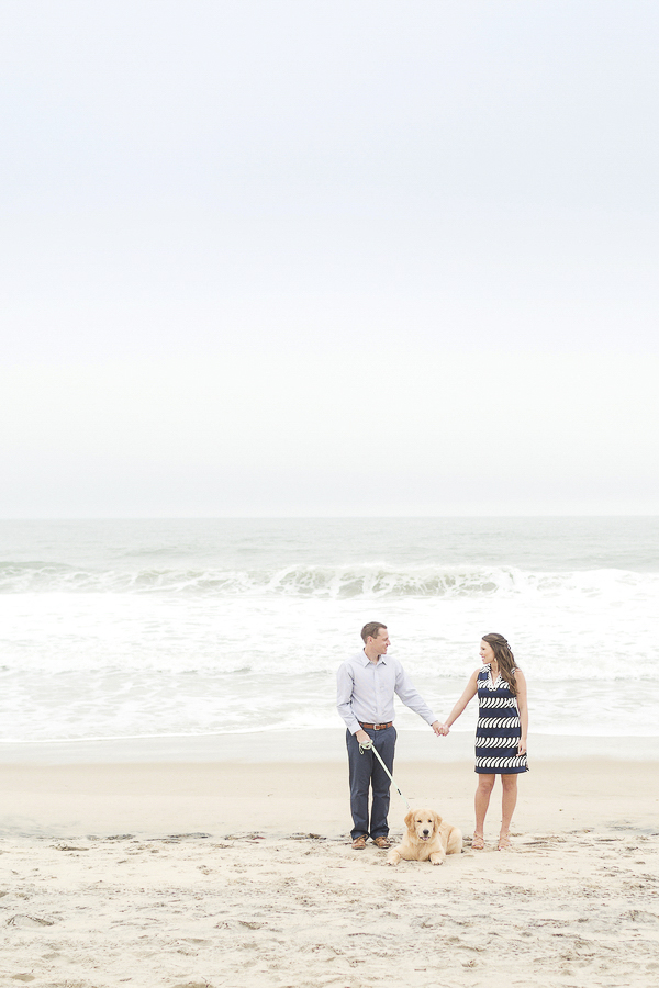 couple holding hands on the beach, dog lying between them ©Anna Grace Photography | Beach engagement photos with dog, Bethany Beach, DE