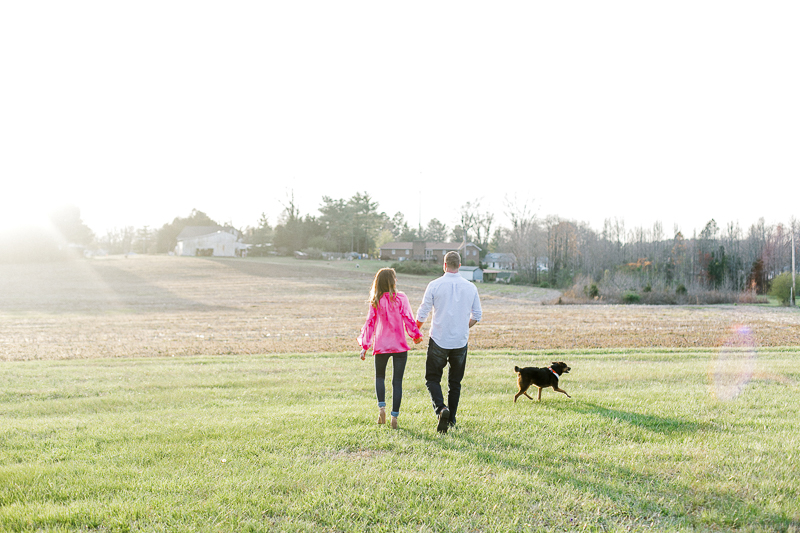 couple walking hand in hand with dog running along them | ©Casey Hendrickson Photography | Charlotte, NC Engagement photos with a dog