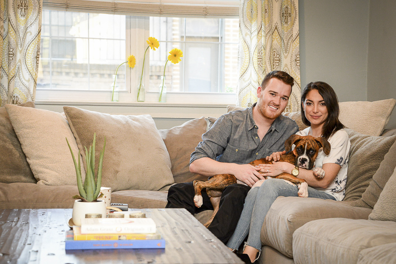 couple sitting on sofa with Boxer puppy in their laps, at home engagement pictures 