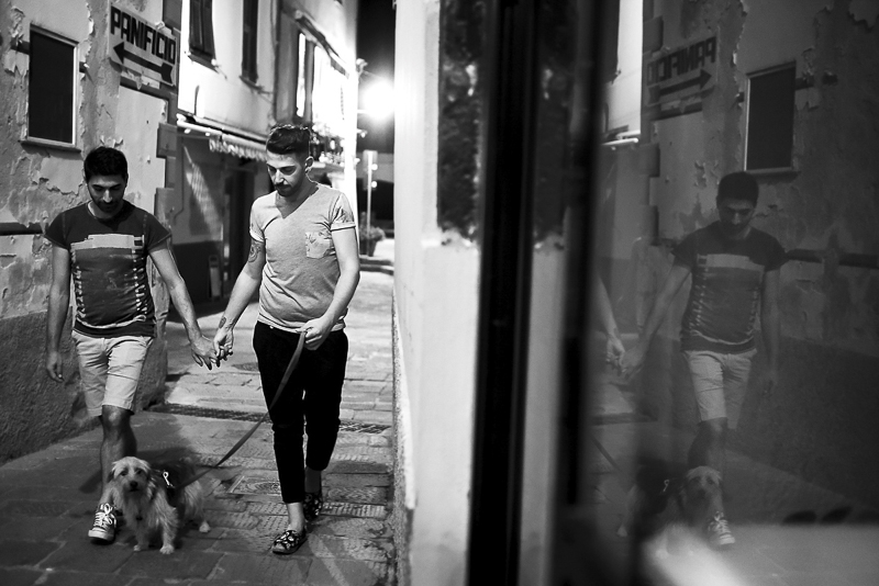 black and white engagement portrait, 2 men holding hands walking their dog through small Italian village