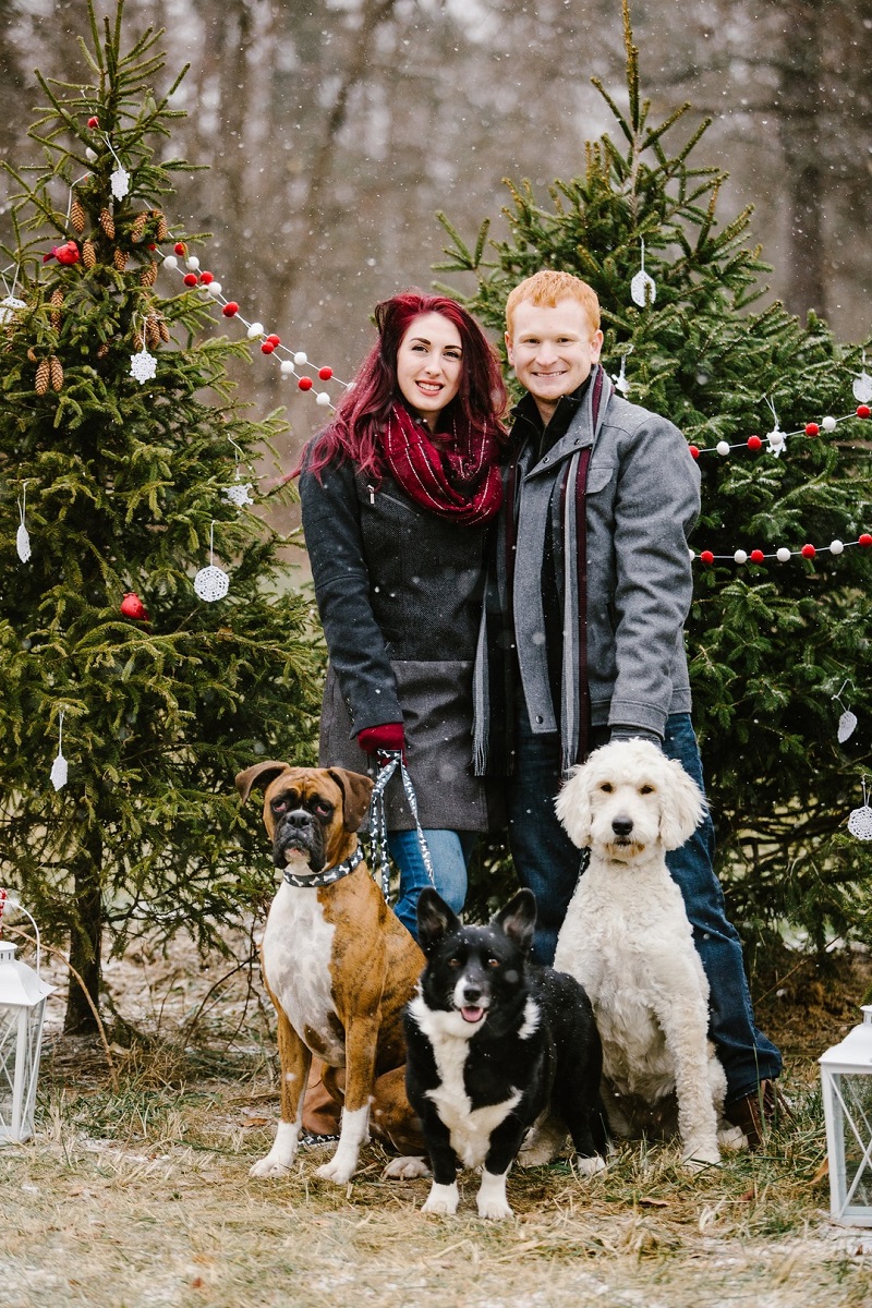 couple and their dogs outside standing by decorated live Christmas trees