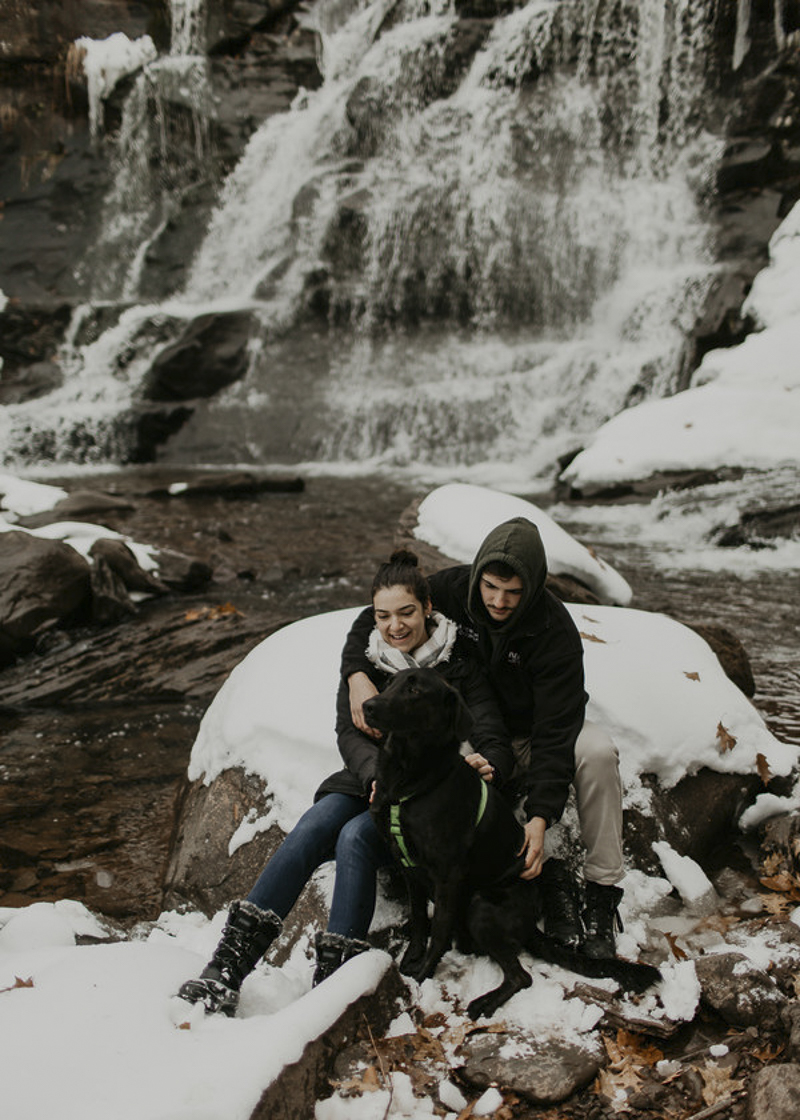 couple and their dog sitting on snow covered boulder in front of waterfall ©Belle La Vie Images | Hudson Valley dog friendly engagement photos 