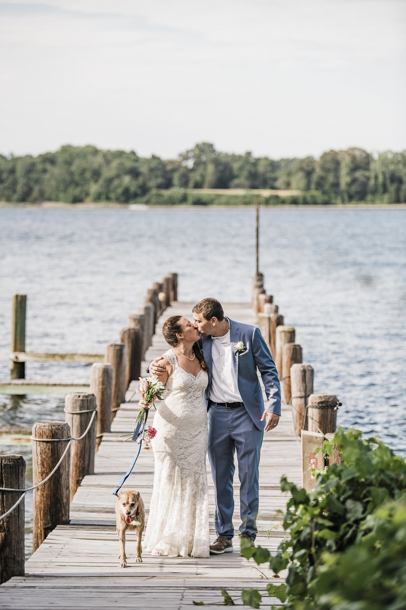 bride and groom kissing on dock with dog at side | ©Landrum Photography 