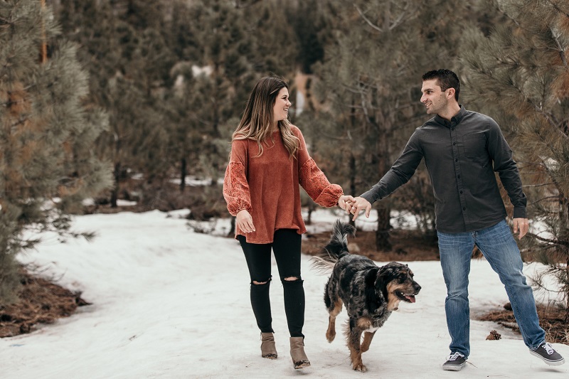©Astray Photography | couple walking hand in hand on the snow while their dog walks in between them