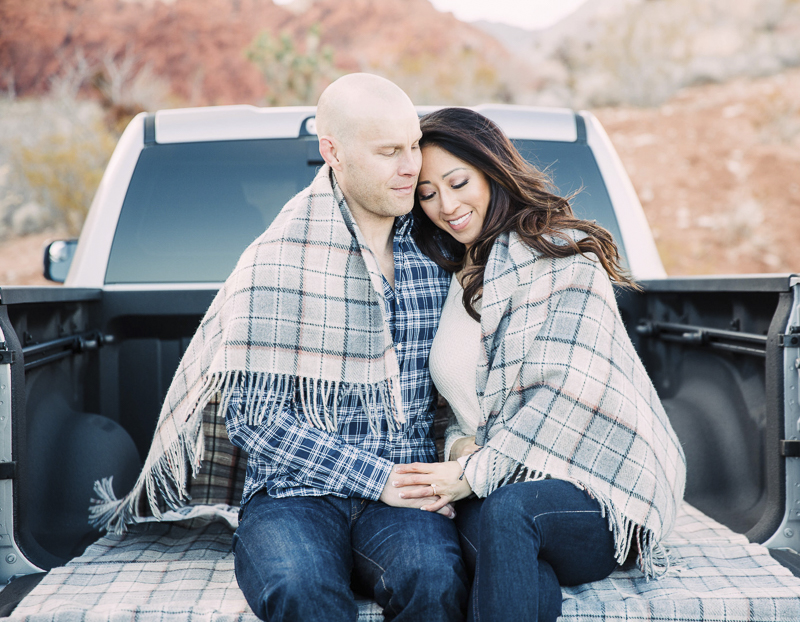 couple sitting in bed of pickup truck with blanket around them, romantic engagement photos | ©Alycia Moore Photography