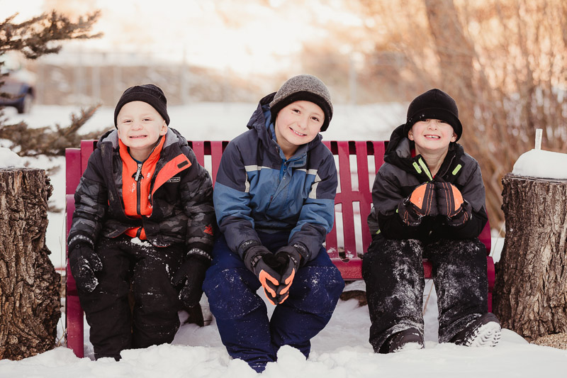 winter family portrait ideas, kid friendly family session, 3 boys sitting on snowy bench | ©Good Morrow Photography