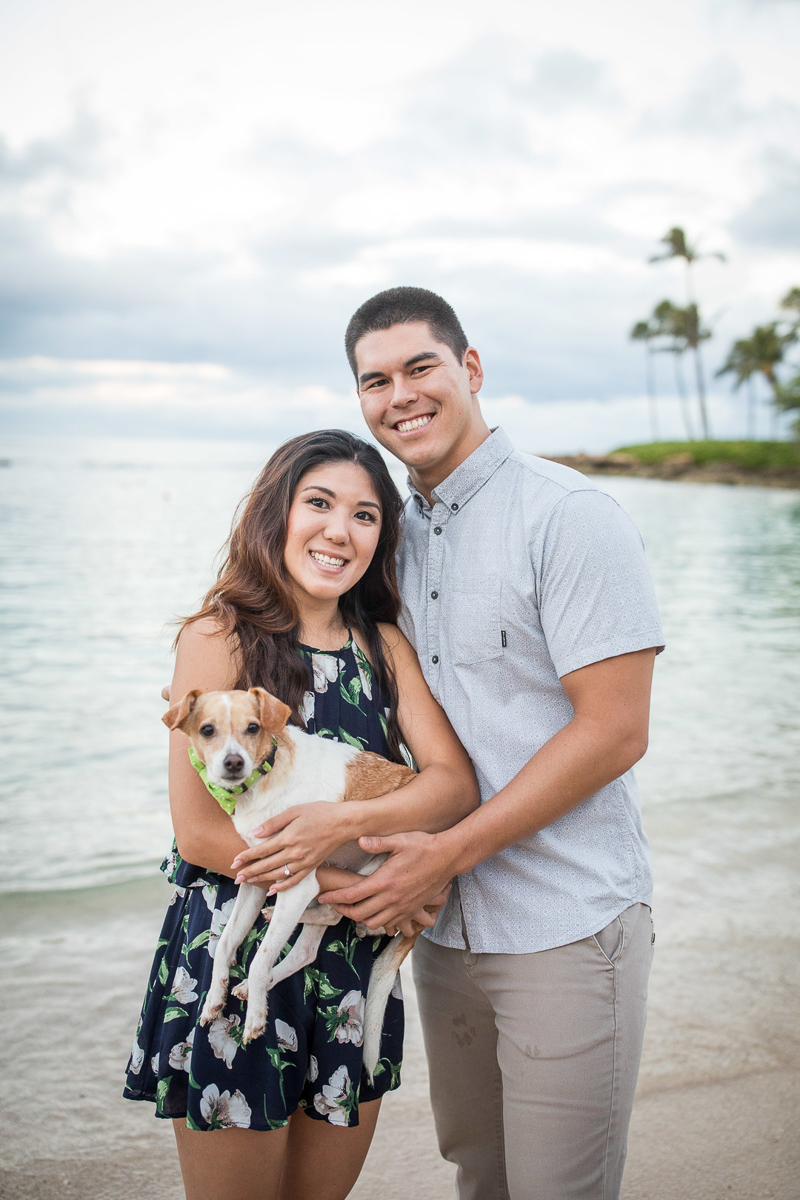 happy couple holding their small dog at water's edge | VIVIDfotos Hawaii engagement and wedding photography