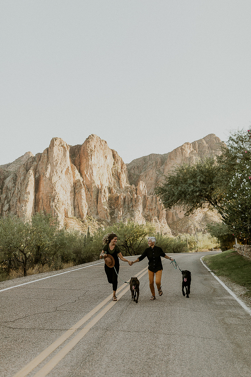women and their dogs running down road, hills in background, ©Kali M Photos | Arizona wedding and elopement photographer
