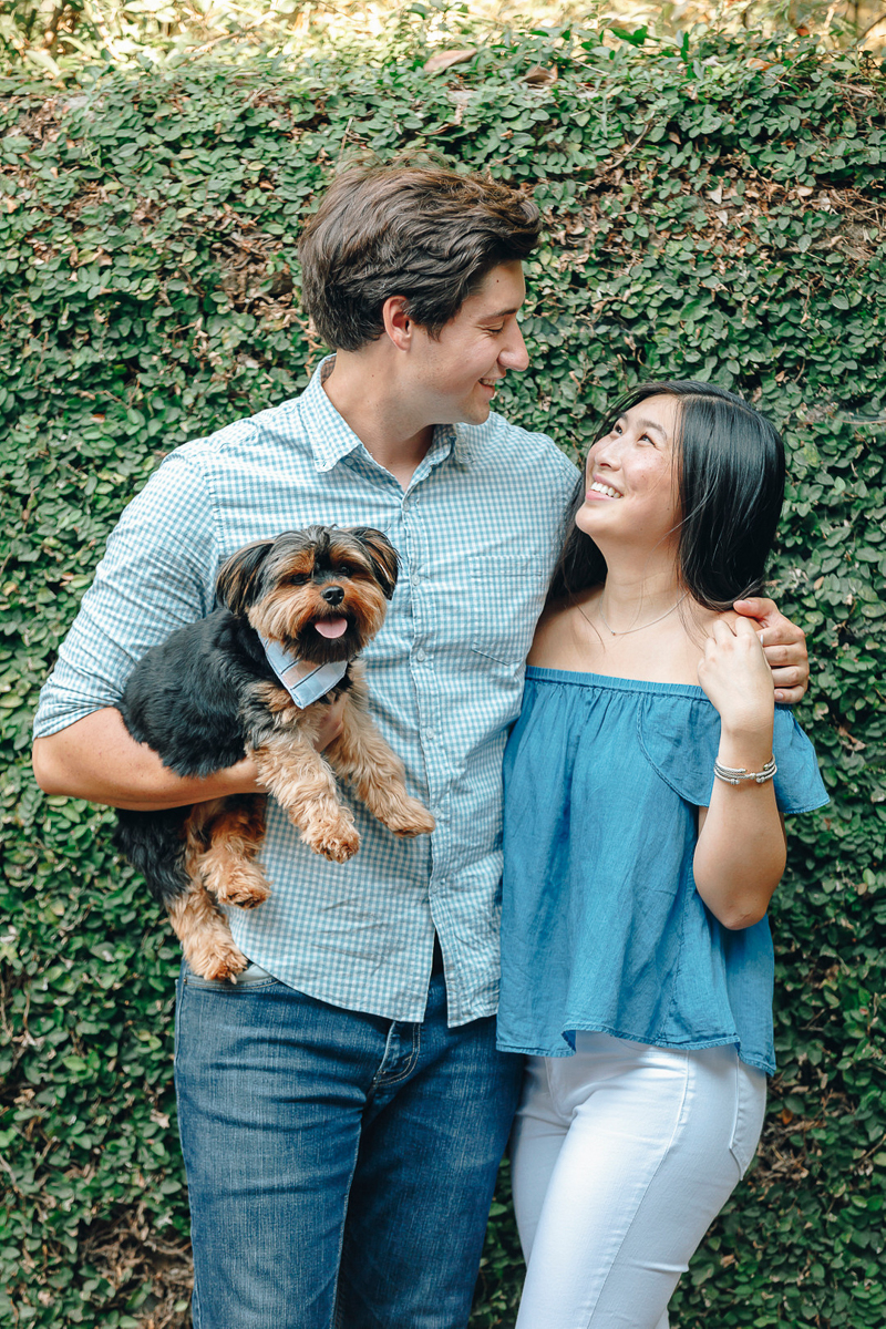 couple standing in front of green hedge and holding Yorkshire Terrier, dog-friendly engagement ideas | ©Charleston Photo Art