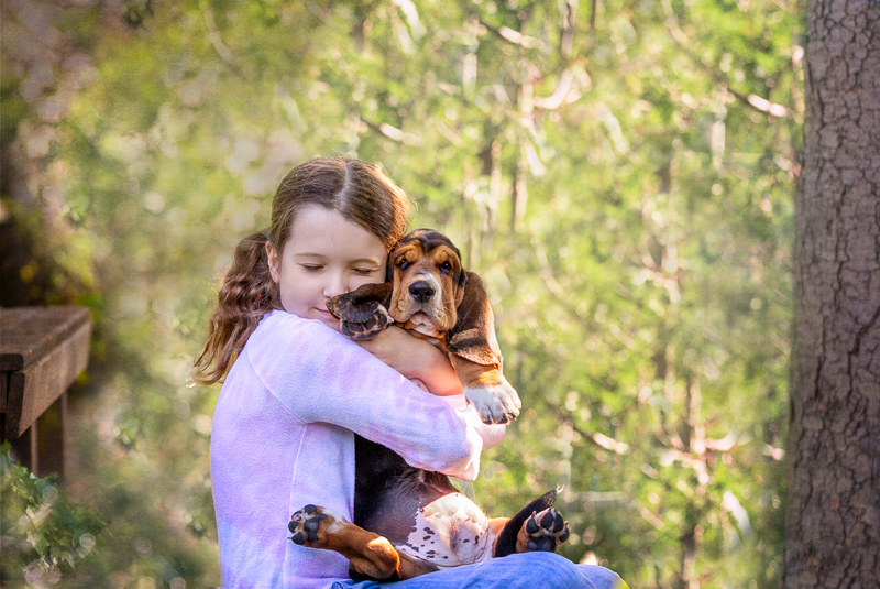 girl hugging her Bassett Hound puppy, love between dogs and kids | ©Terri J Photography