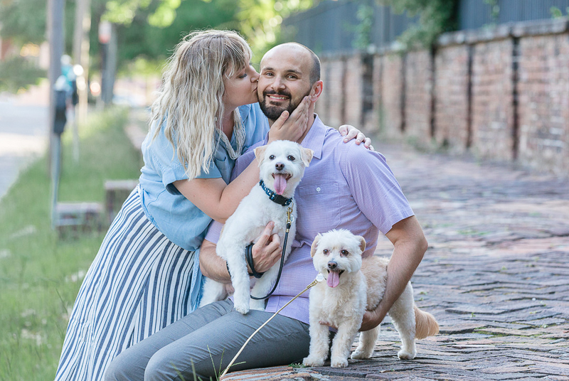 woman kissing man sitting on old brick road with dogs, ©Charleston Photo Art, dog-friendly family portraits 