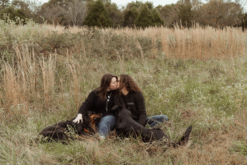 couple kissing in a field with dogs in their laps | dog-friendly engagement session | ©Emily Swan Photography 