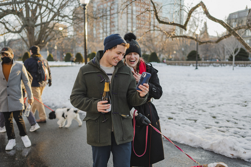 couple celebrating winter proposal, face-timing and holding champagne bottle | ©Amanda Macchia Photography | dog-friendly marriage proposal