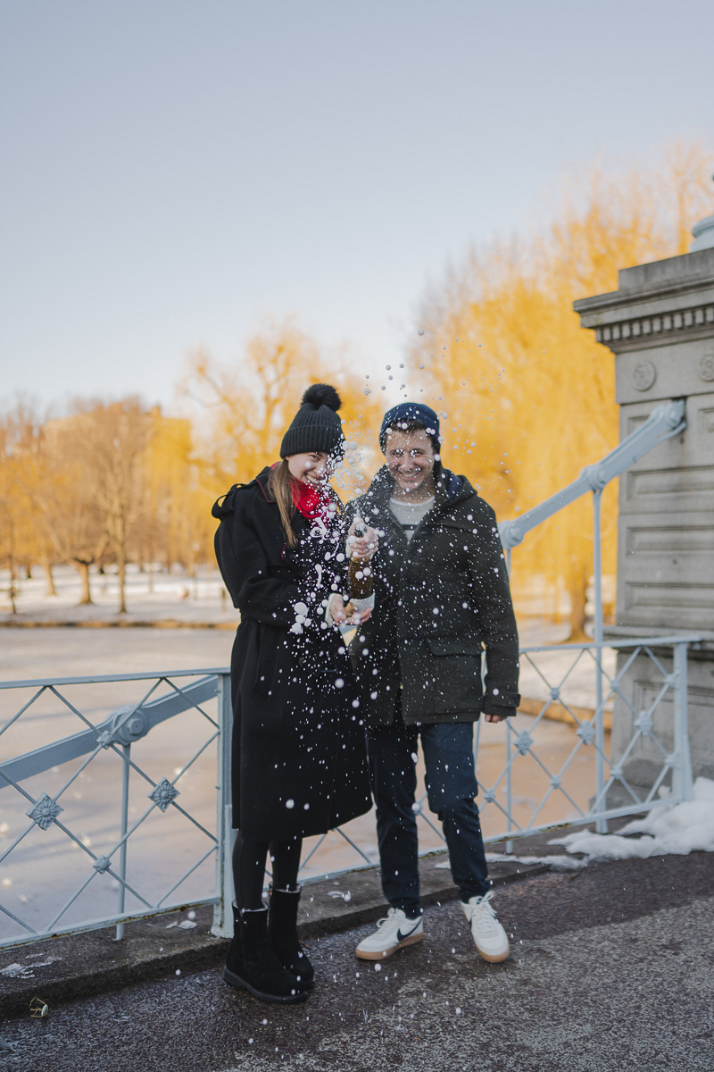 couple celebrating winter marriage proposal with champagne | ©Amanda Macchia Photography | Boston, MA