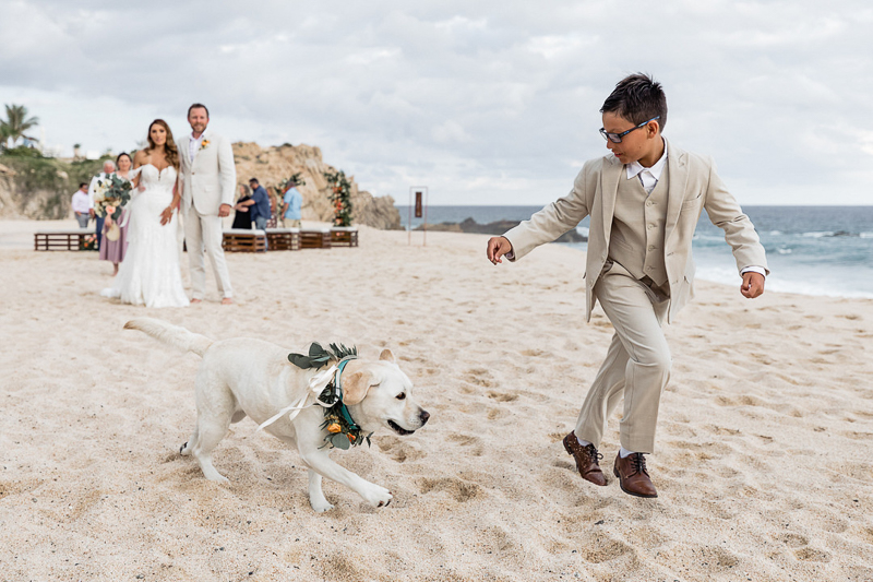 Labrador Retriever running with little boy wearing a suit on the beach, dog-friendly wedding | ©Fabi Rosas Wedding Photography