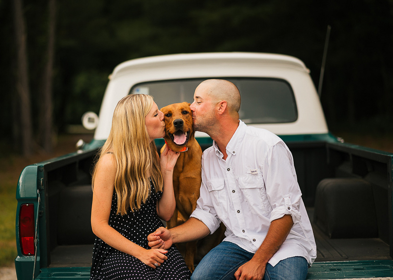 couple holding hands while kissing their dog in back of vintage pickup truck | ©Memories by Lexi