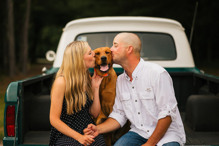 couple holding hands while kissing their dog in back of vintage pickup truck | ©Memories by Lexi
