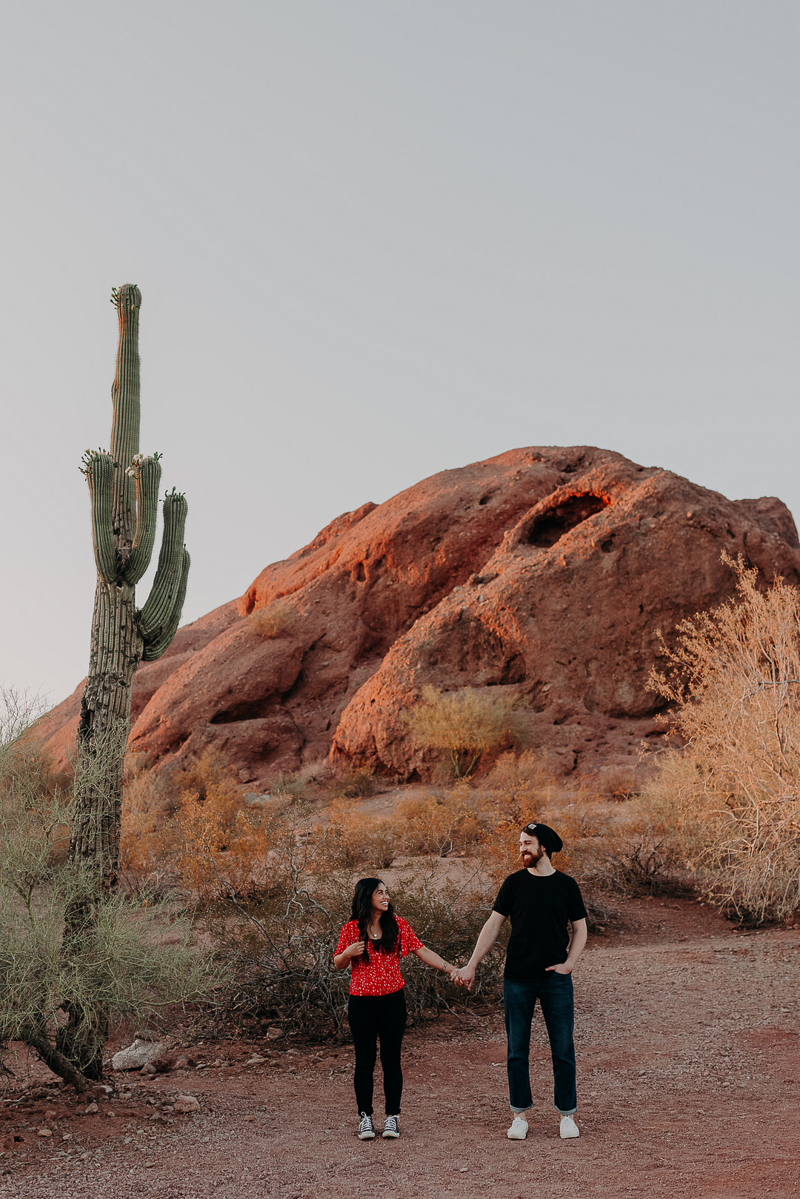 desert engagement photos, Papago Park, Tempe, AZ | woman wearing red top, hugging man in black shirt and black beanie | ©Suzy Goodrick Photography