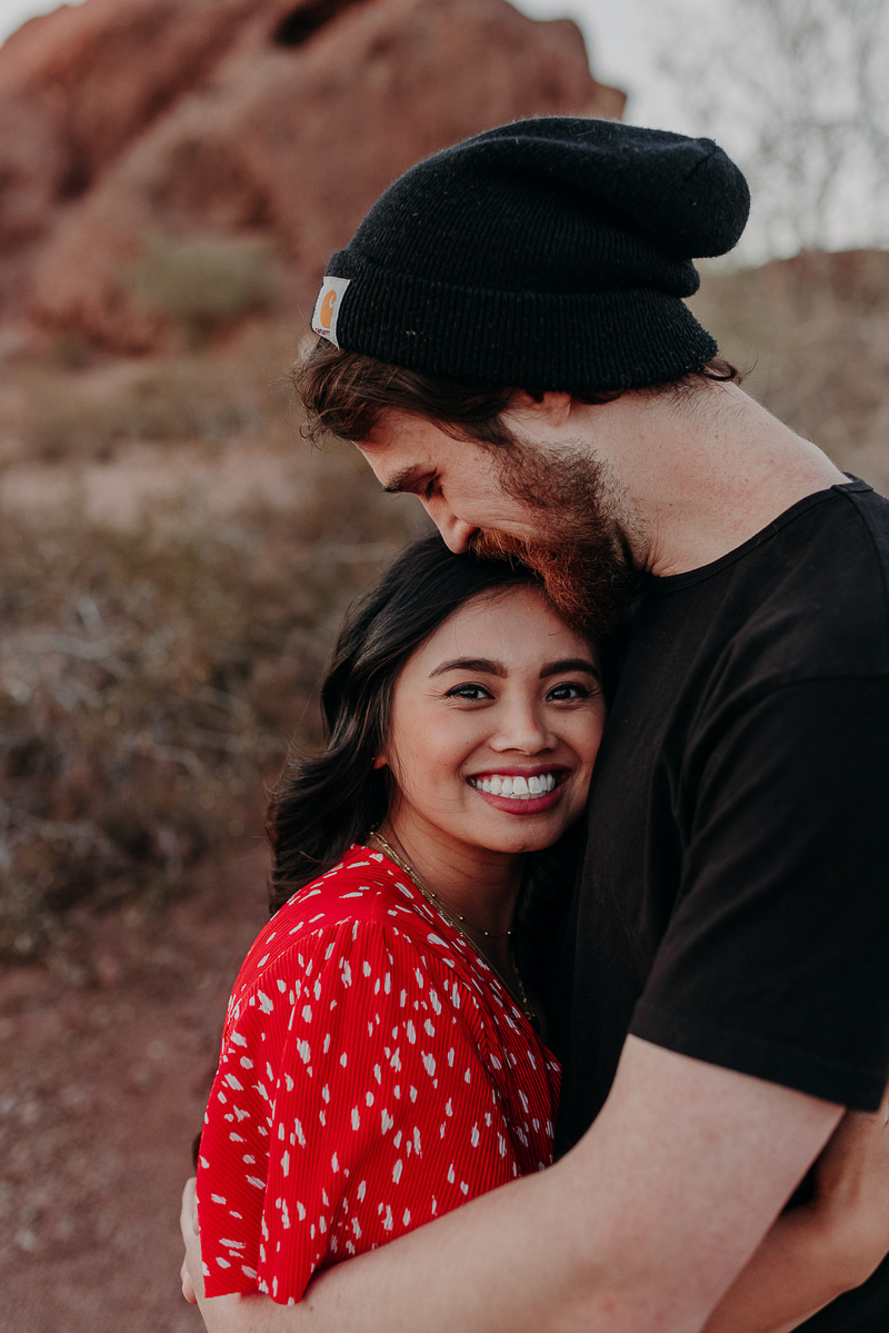 woman wearing red top, hugging man in black shirt and black beanie | desert engagement photos ©Suzy Goodrick Photography