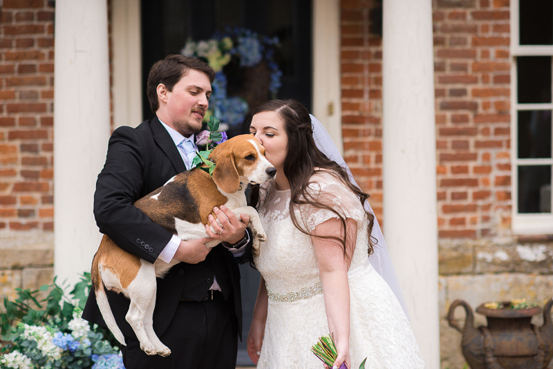 man holding beagle while bride kisses the dog in front of Westenhanger Castle, wedding photos with dog | ©fleur challis photography 