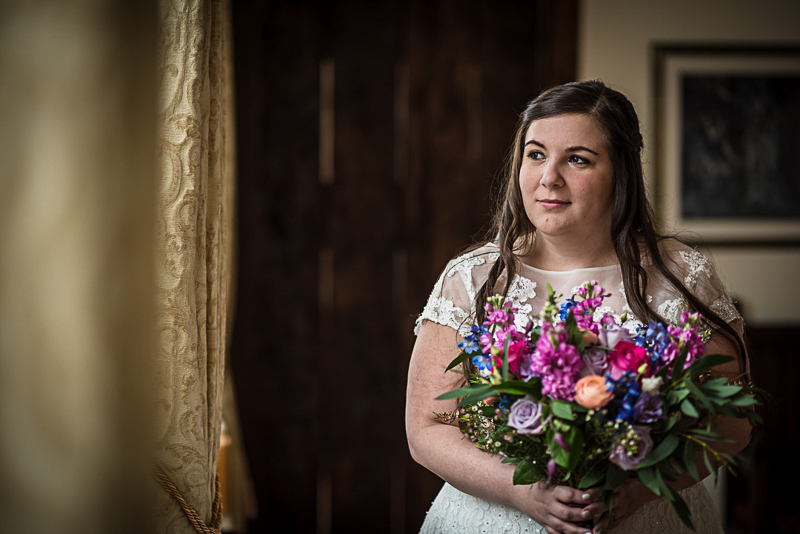 bride holding vibrant bouquet while standing near window,| ©fleur challis photography 