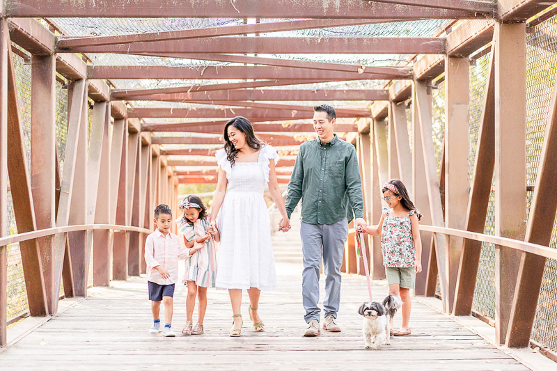 family holding hands and walking small dog on cool bridge| ©Laura Michele Photography, San Jose dog-friendly family portraits