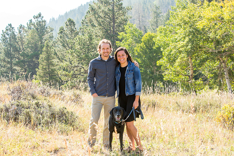 couple standing with their Black Lab in field with mountains in background, dog-friendly family photos, ©Nichole Emerson Photography | Estes Park, CO 