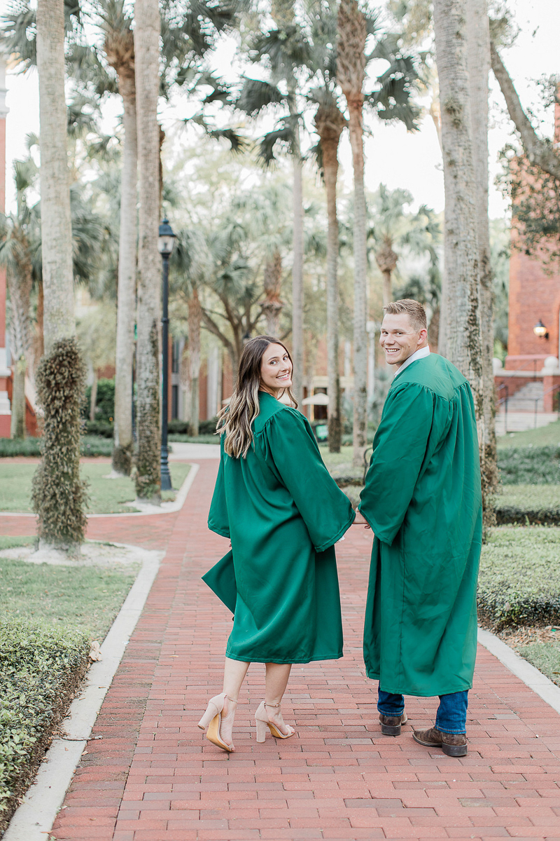 couple wearing green graduation robes holding small dog | ©Willow & Oak Photography