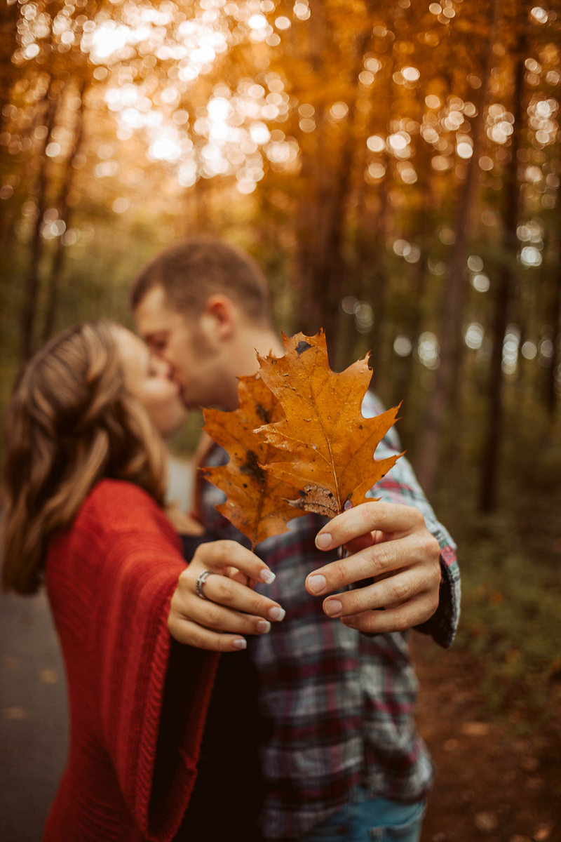 couple kissing and holding oak leaves, fall engagement portraits ©OnFaith Photography