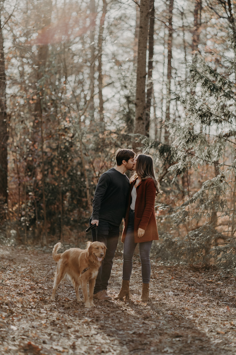 couple standing and kissing with dog next to them, romantic late fall engagement session, Roswell, GA ©Nathalia Frykman Photography