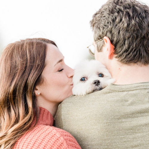 dog-friendly engagement session ideas, woman kissing dog that is snuggling against man's shoulder ©Mel Schroeder Photography